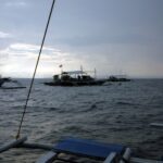 Tre banca-båter for dykking ligger for anker på Monad Shoal under en grå morgenhimmel, sett fra dekket på en annen båt