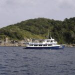 En blå og hvit safaribåt ankret foran en av Similan-øyene, med grå granittblokker i vannkanten under skogen