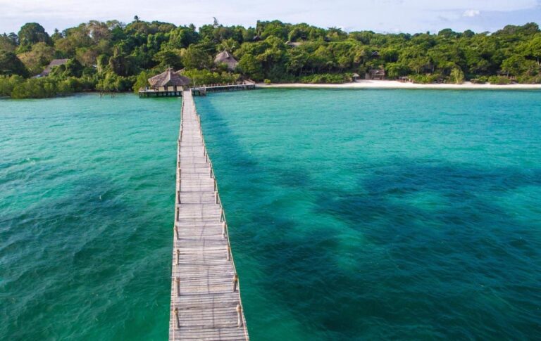 Den lange trebrygga på Fundu Lagoon over det turkise vannet, mot den skogkledde kysten