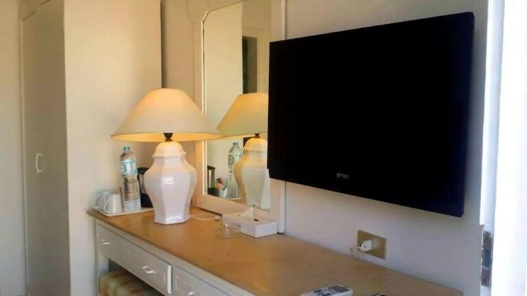 En kommode med en hvit lampe, et speil og en veggmontert TV