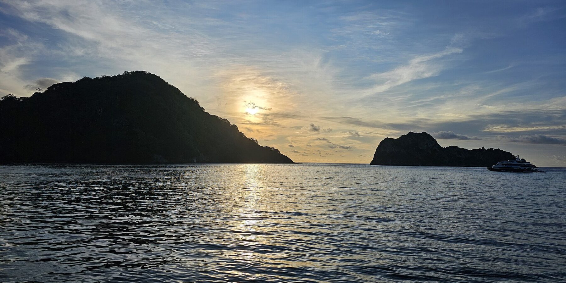 Cocos Island i motlys ved solnedgang, med en dykkesafaribåt for anker til høyre og rolig hav