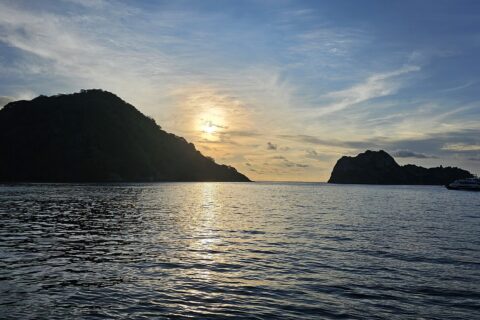 Cocos Island i motlys ved solnedgang, med en dykkesafaribåt for anker til høyre og rolig hav