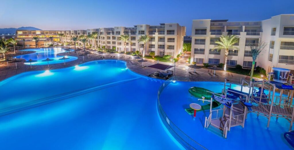 De opplyste bassengene på JAZ Soma Beach i skumringen, mellom bygningene og palmene
