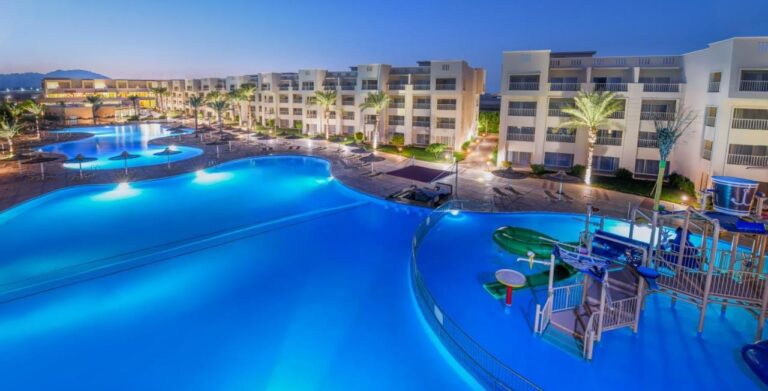 De opplyste bassengene på JAZ Soma Beach i skumringen, mellom bygningene og palmene