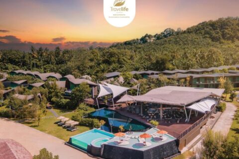 Flyfoto av Kalima Resort Khao Lak i solnedgang, med bassengene og de buede takene ved foten av en skogkledd ås