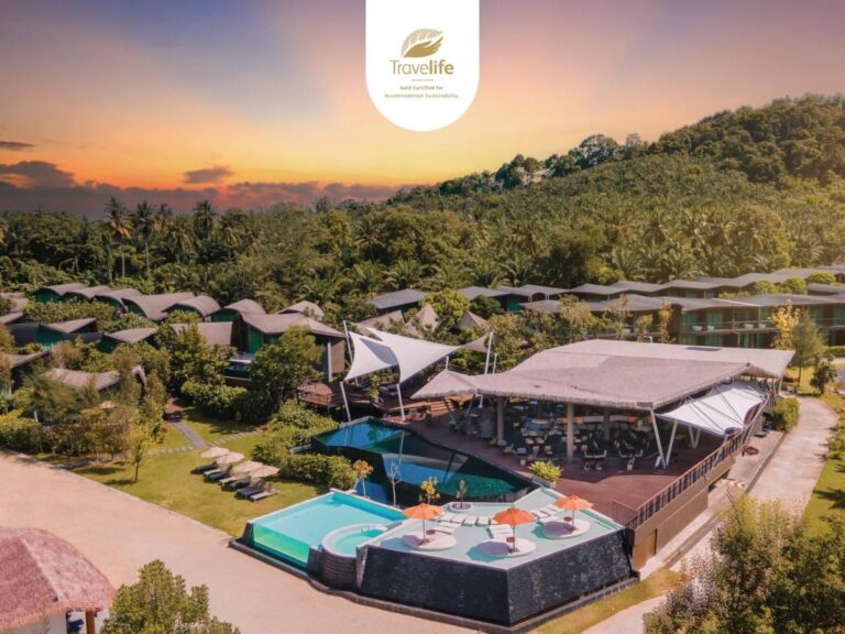 Flyfoto av Kalima Resort Khao Lak i solnedgang, med bassengene og de buede takene ved foten av en skogkledd ås