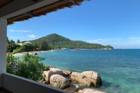 Bukta og klippene sett fra en overbygd terrasse på Koh Tao Heritage, med båter for anker