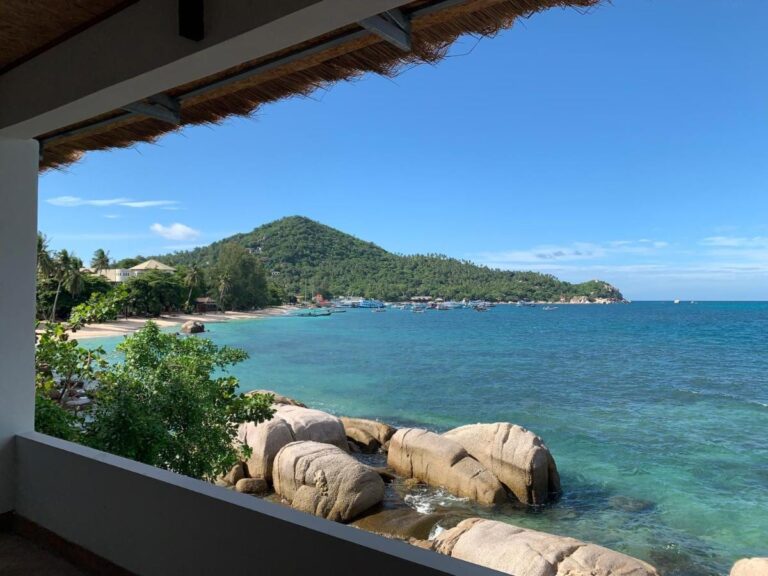 Bukta og klippene sett fra en overbygd terrasse på Koh Tao Heritage, med båter for anker