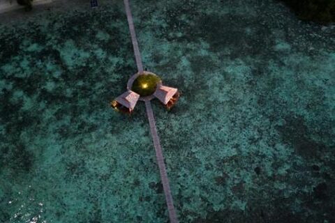 Flyfoto om natten av en lang trebrygge fra stranden, med to hytter på påler halvveis ute