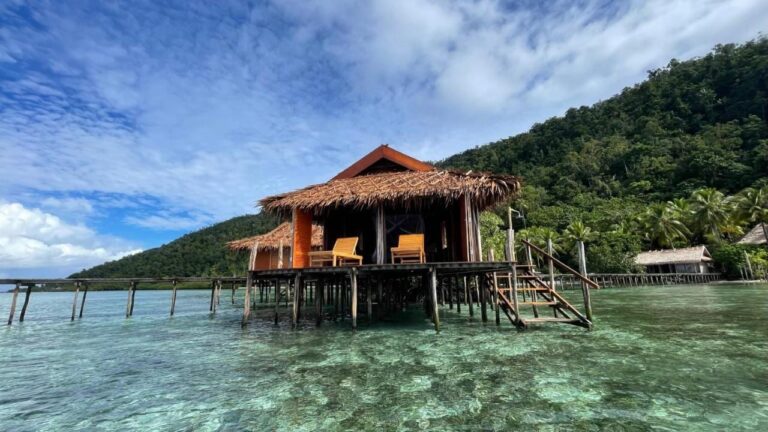 En bungalow ved Nyande Raja Ampat på påler, over klart vann, ved foten av en skogkledd ås