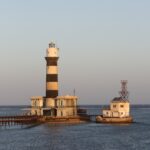 Fyrtårnet på Daedalus, et tårn med svarte og hvite striper på revet, med bygninger og en metallbrygge, i solnedgang