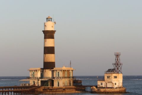 Fyrtårnet på Daedalus, et tårn med svarte og hvite striper på revet, med bygninger og en metallbrygge, i solnedgang
