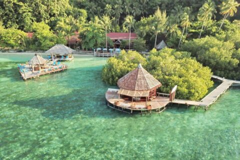 Raja Ampat Dive Lodge sett fra luften, med bryggene på påler og de røde takene under palmene