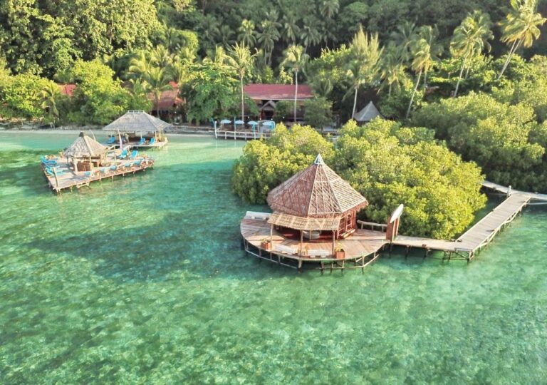 Raja Ampat Dive Lodge sett fra luften, med bryggene på påler og de røde takene under palmene