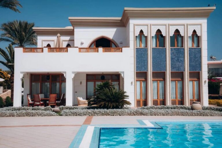 En hvit bygning på Reef Oasis Beach Resort, med buede vinduer og blå mosaikkpaneler, foran et basseng
