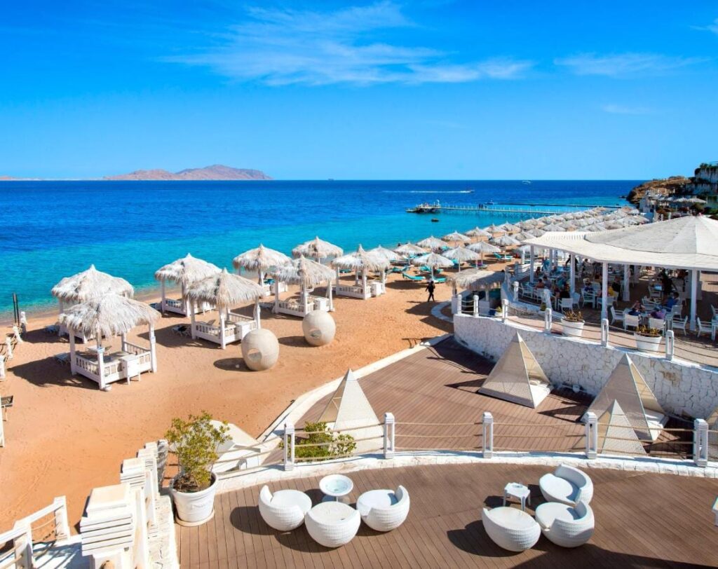 Stranden på Sunrise Arabian Beach Resort, med parasoller av strå og brygga, rett overfor Tiran-øya