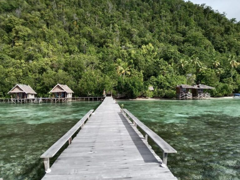 En lang brygge med benker som fører inn til land, mellom bungalowene på Terimakasih Homestay