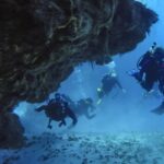 Fire dykkere kommer ut av en koralltunnel over sandbunn på Cozumel, med steintaket over seg