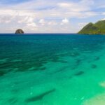Flyfoto av den lange stranden i Le Diamant omkranset av turkist vann, med Rocher du Diamant ute i sjøen og Morne Larcher, en grønn ås, til høyre