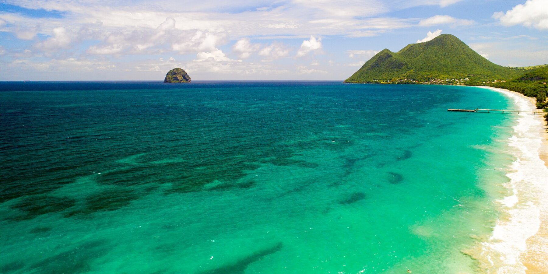 Flyfoto av den lange stranden i Le Diamant omkranset av turkist vann, med Rocher du Diamant ute i sjøen og Morne Larcher, en grønn ås, til høyre