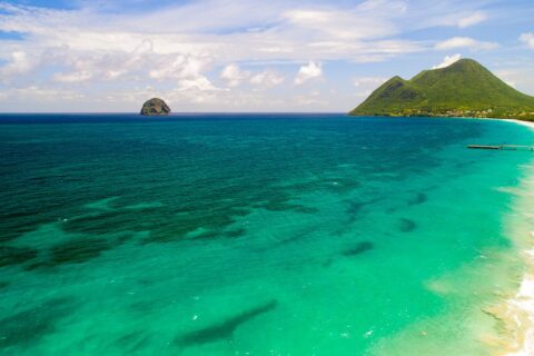 Flyfoto av den lange stranden i Le Diamant omkranset av turkist vann, med Rocher du Diamant ute i sjøen og Morne Larcher, en grønn ås, til høyre