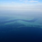 Flyfoto av en mørkeblå S-formet kanal som slynger seg mellom de turkise revflatene i barriererevet, med noen små hvite båter i passet