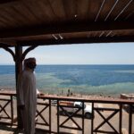 Fra en treterrasse ser en mann i galabeya ut over bassenget i Blue Hole, kantet av lyst rev, der folk bader